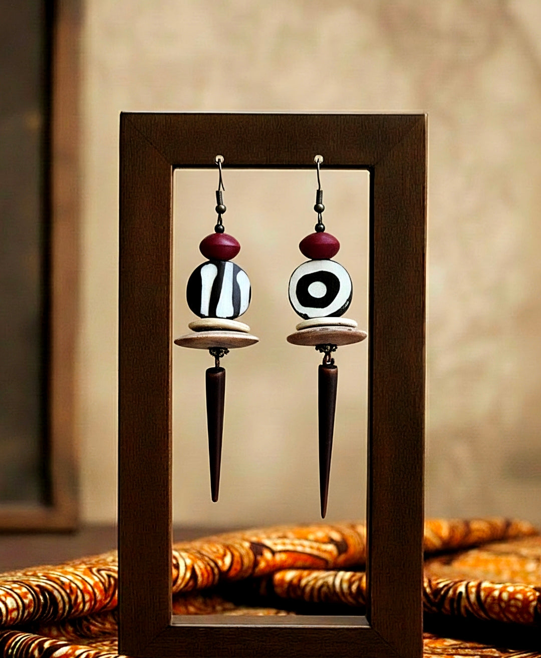 Pair of ethnic earrings with black, white, and red design in a wooden frame.