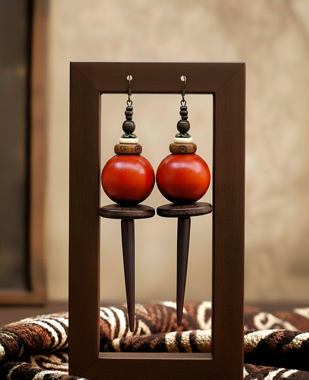 Pair of orange earrings with black and gold accents displayed in a wooden frame.