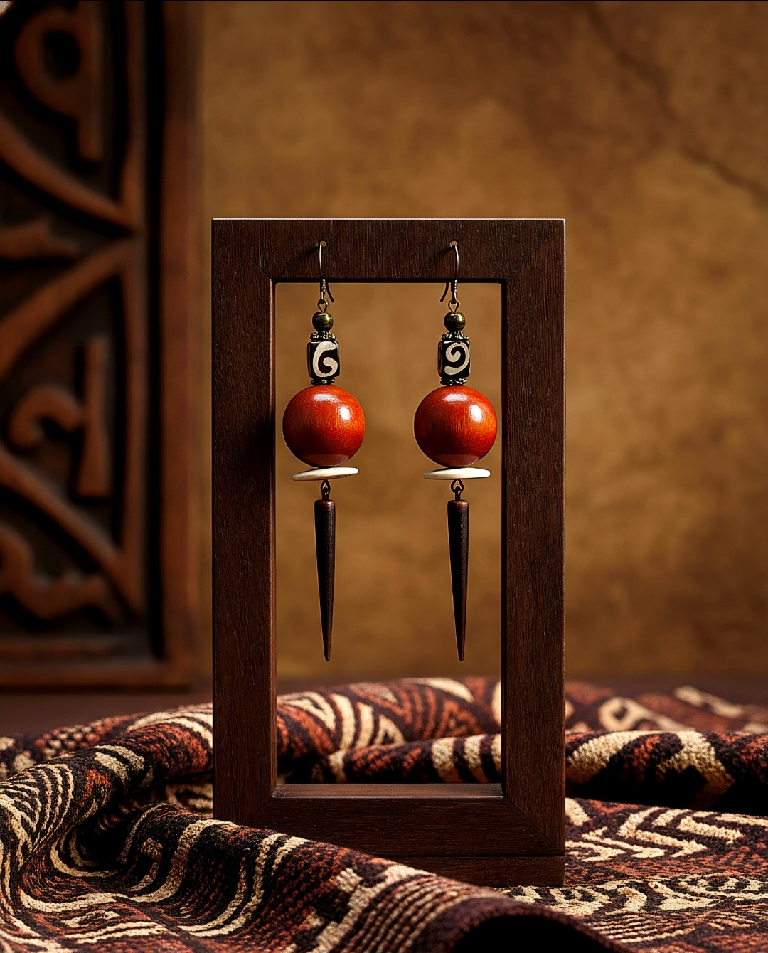 Pair of earrings with orange spherical beads and metallic spikes displayed in a wooden frame.