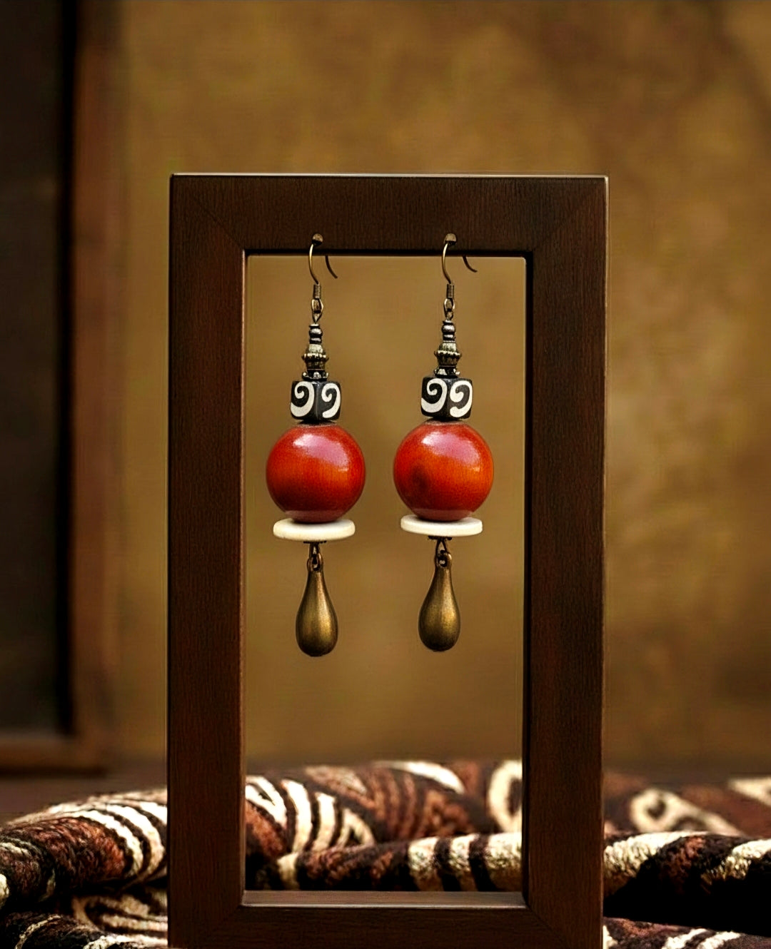 Pair of  orange wood earrings with gold accents in a wooden frame.