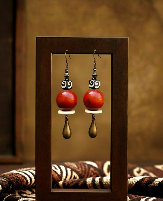 Pair of  orange wood earrings with gold accents in a wooden frame.