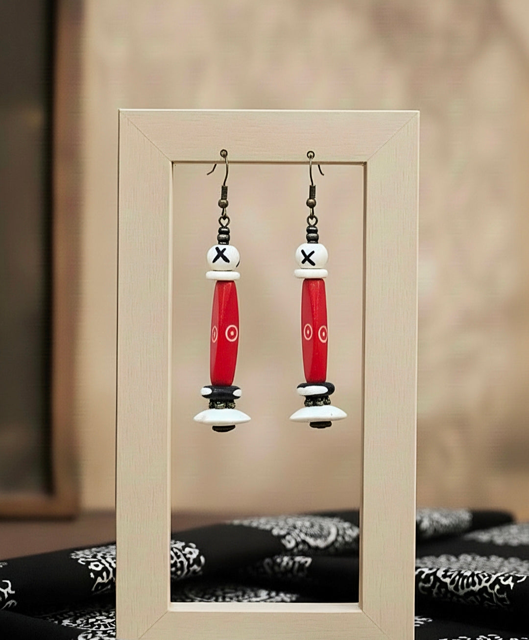 Pair of red and white earrings displayed in a wooden frame.
