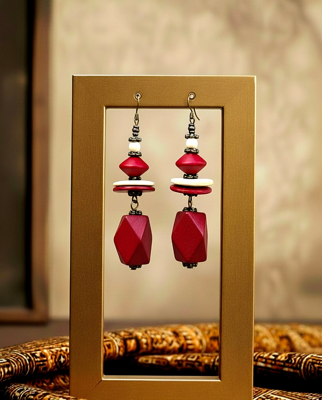 Red beaded wood earrings displayed in a gold frame against a neutral background
