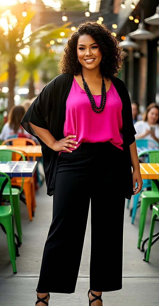 Woman in a pink top and black cardigan standing outdoors with tables and chairs in the background.