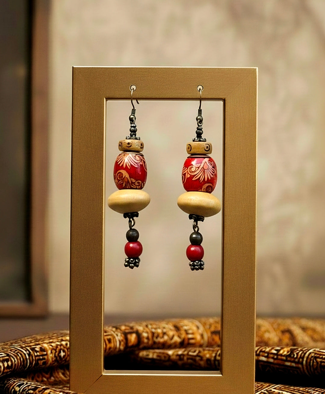 Pair of decorative red earrings with red and beige beads in a wooden frame.