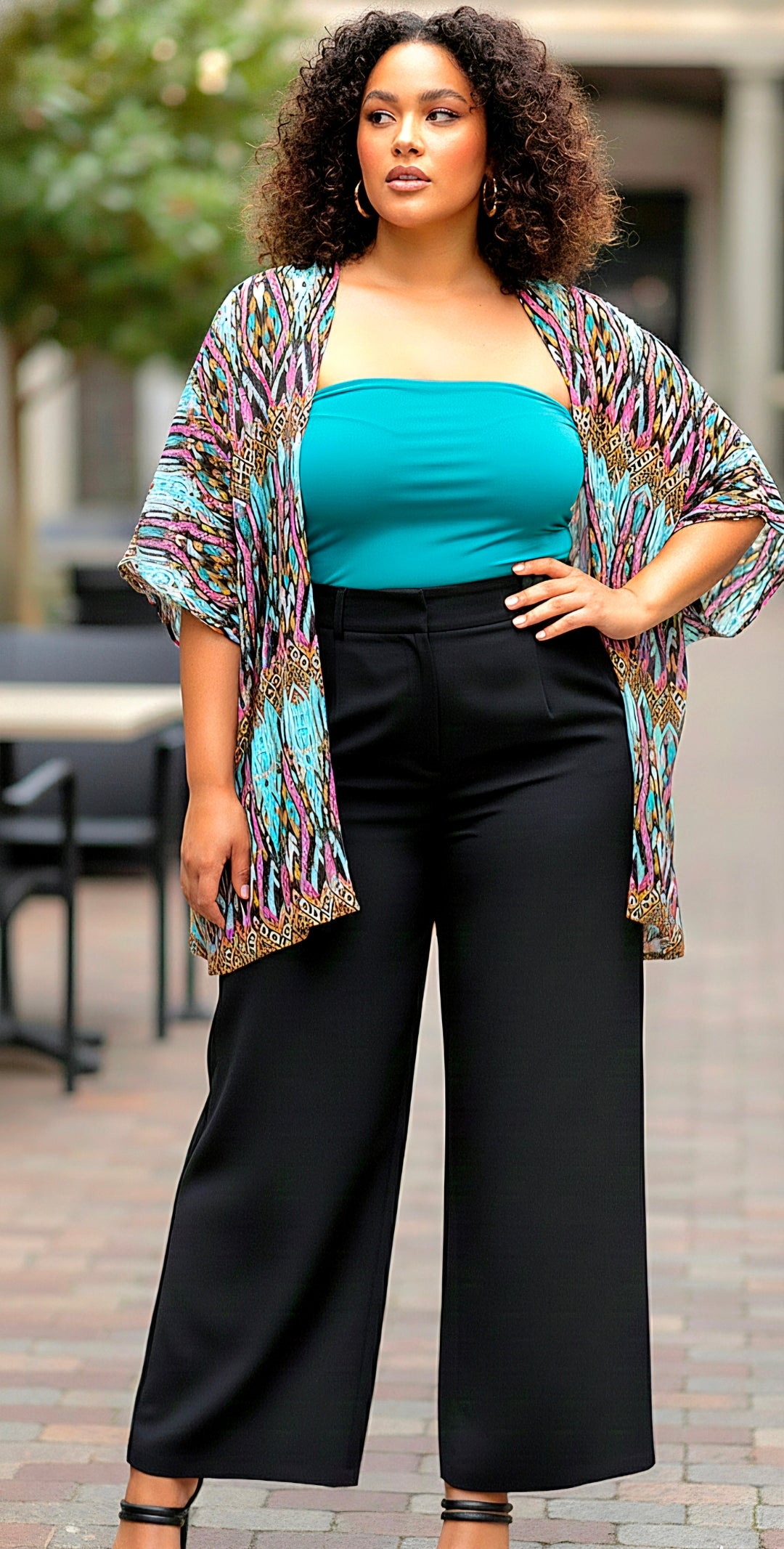 Woman wearing a colorful kimono over a teal top and black pants outdoors.