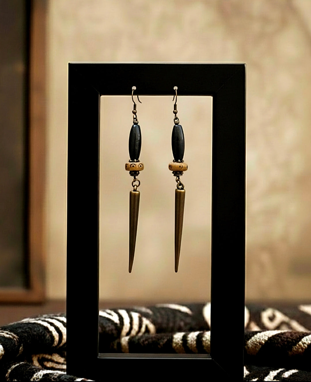 Pair of earrings with long, pointed drops on a reflective surface.