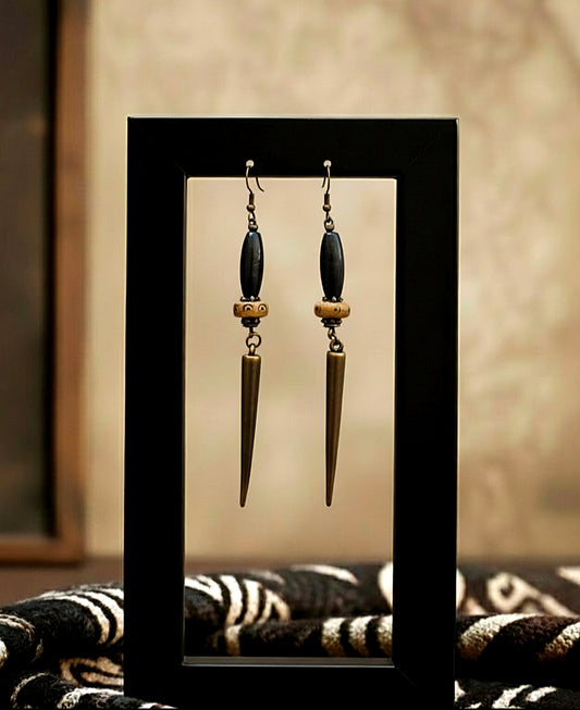 Pair of earrings with long, pointed drops on a reflective surface.