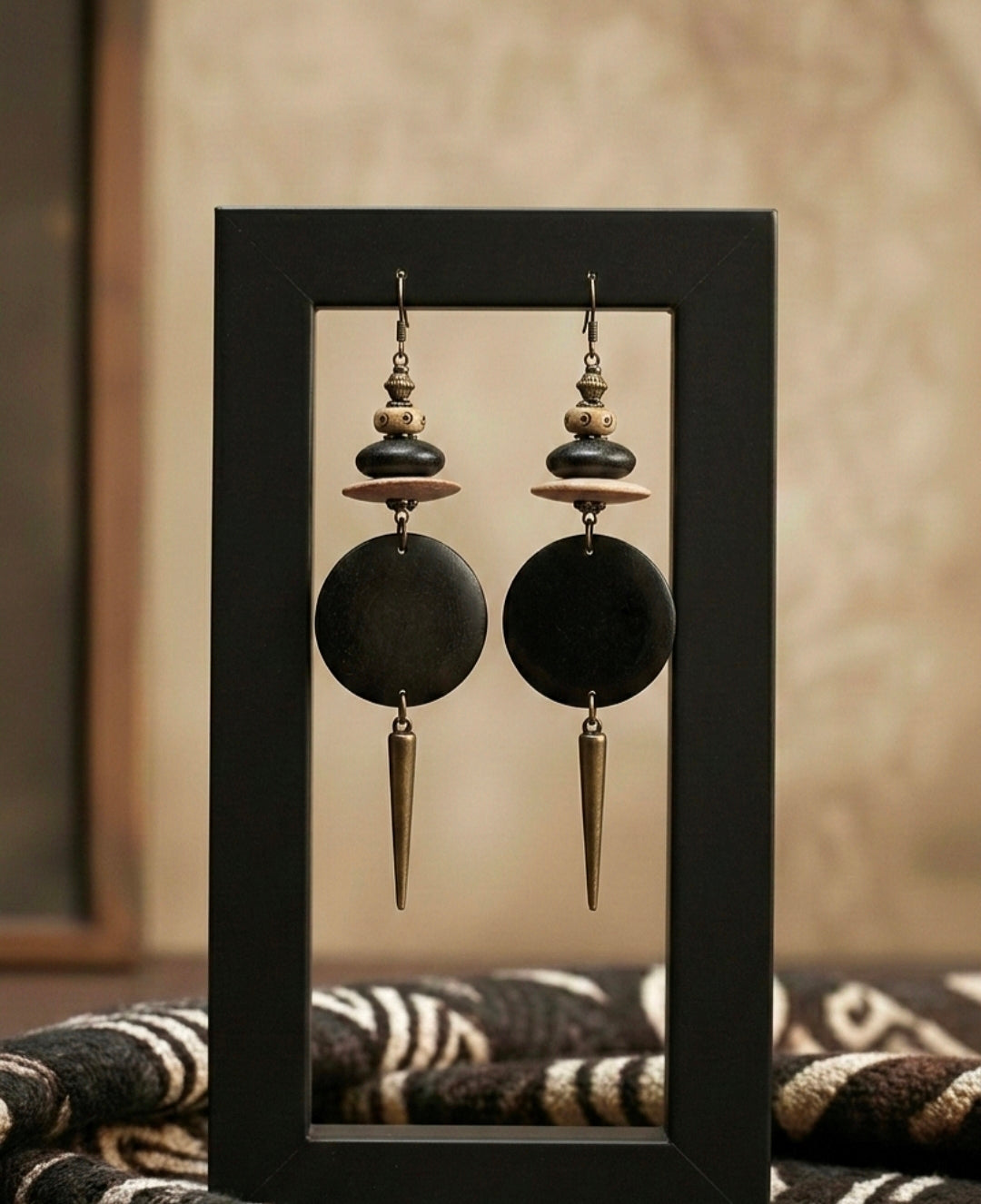 Pair of black and gold earrings in a black frame on a textured surface.