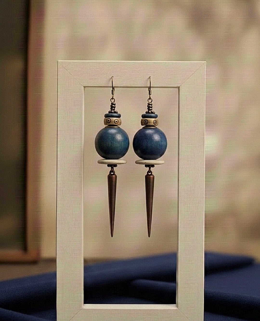 Pair of blue spherical earrings with bronze spike designs displayed in a light wooden frame.