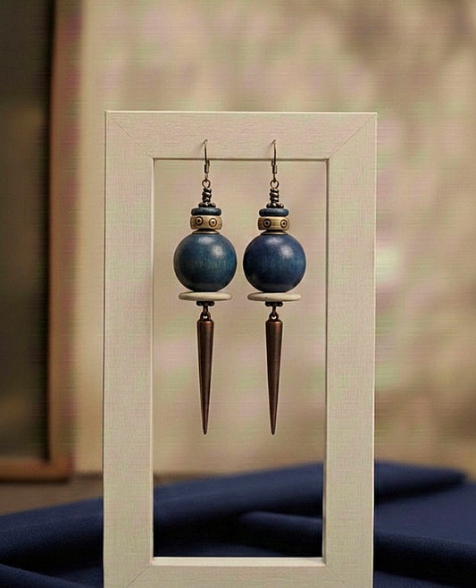 Pair of blue spherical earrings with bronze spike designs displayed in a light wooden frame.
