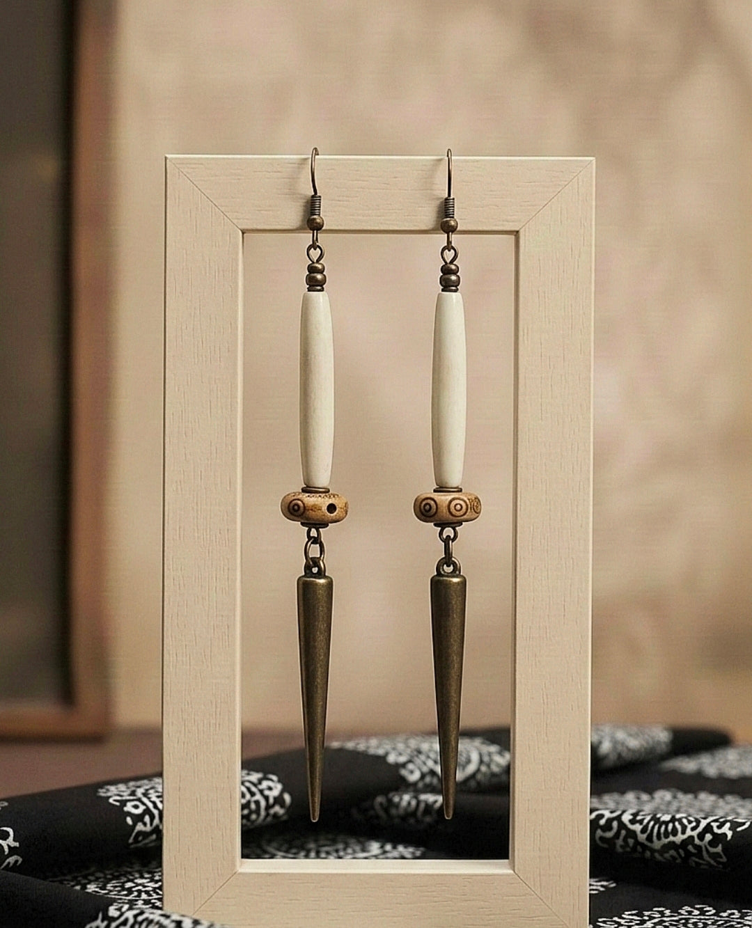 Pair of earrings with long, thin, metallic hooks displayed against a neutral background.