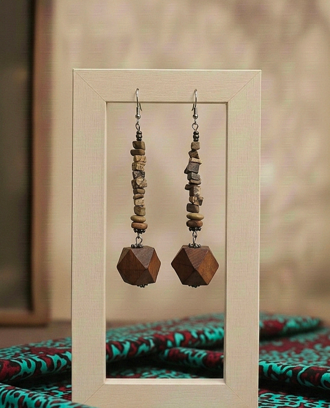 Pair of wooden beaded earrings displayed in a frame with a patterned fabric background.