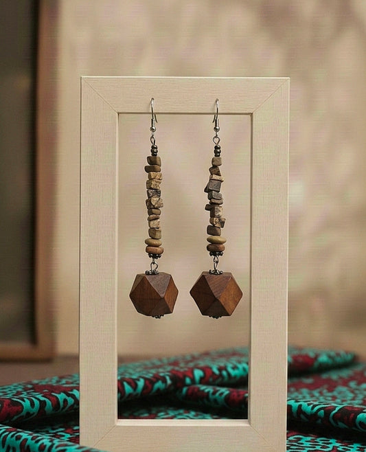 Pair of wooden beaded earrings displayed in a frame with a patterned fabric background.