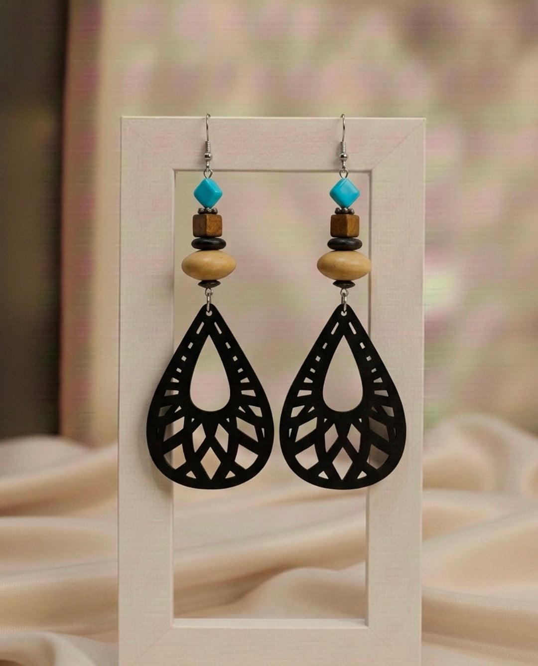 Black lace-style earrings with wooden and turquoise beads on a beige background