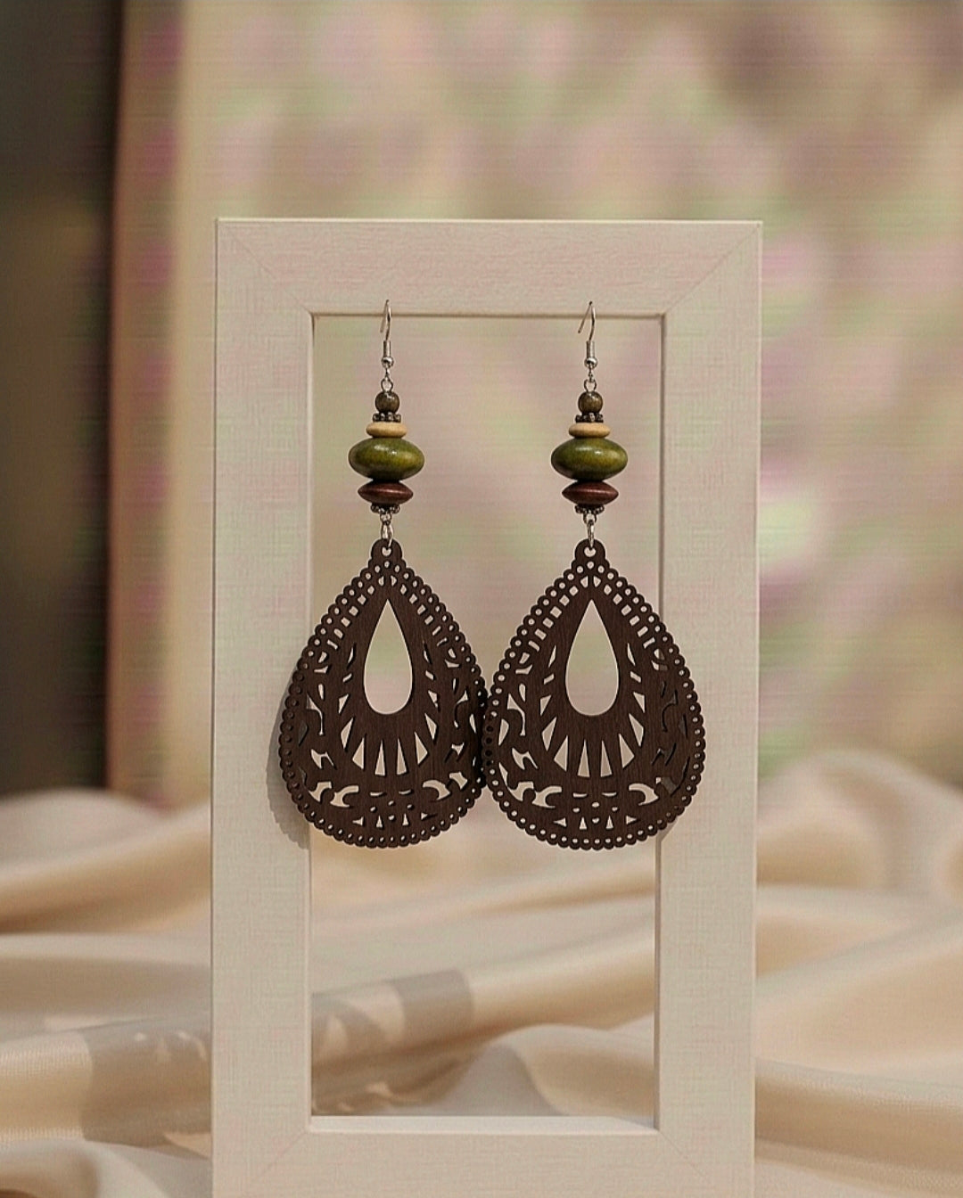 Pair of ornate earrings with green beads on a beige background