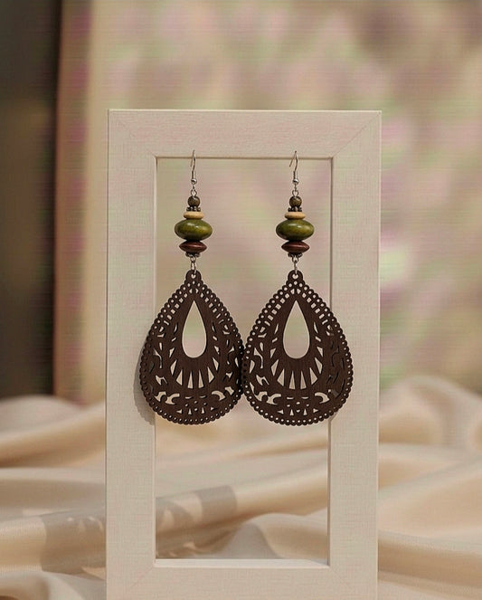 Pair of ornate earrings with green beads on a beige background