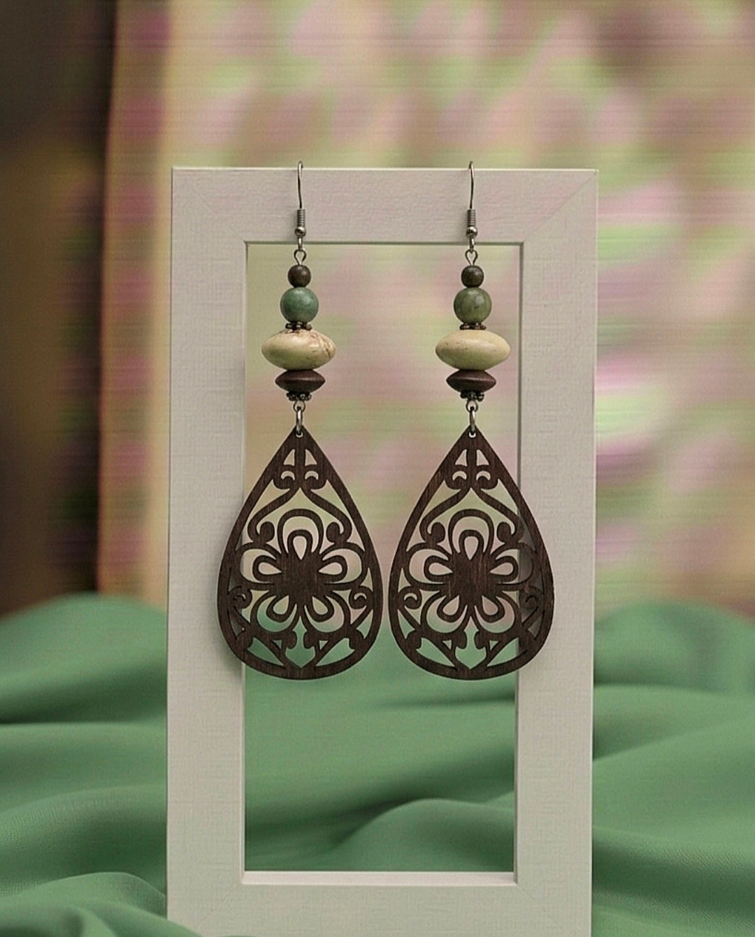 Pair of ornate earrings with floral designs on a green fabric background