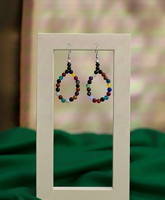Colorful beaded earrings displayed on a stand with a blurred green background