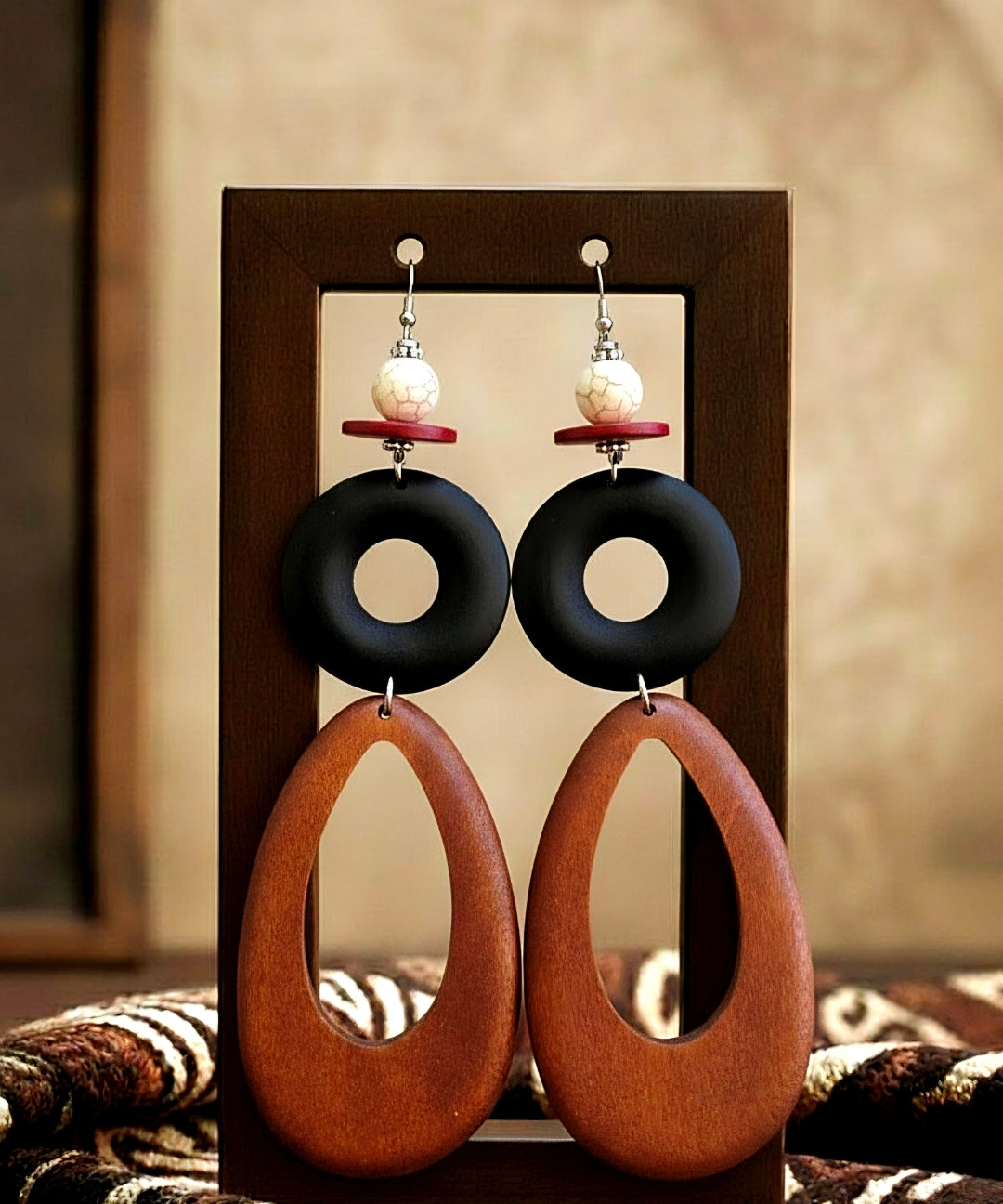 Pair of wood earrings with black and brown circular designs on a wooden stand.