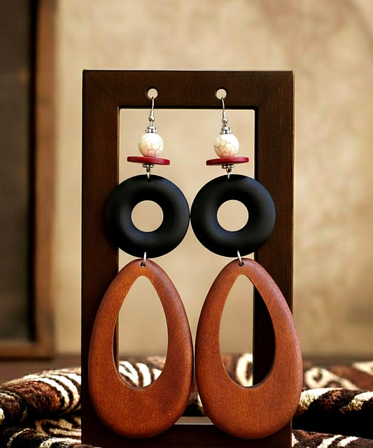 Pair of wood earrings with black and brown circular designs on a wooden stand.