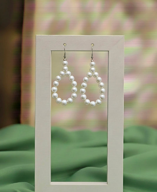 Pearl drop earrings displayed on a stand with a blurred floral background