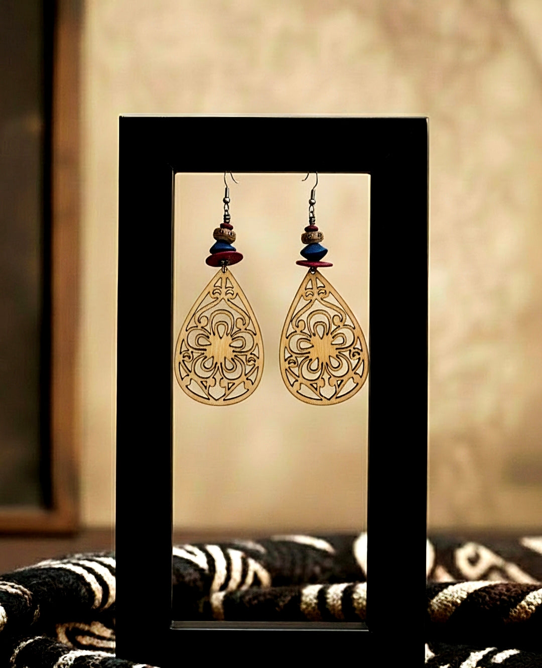 Pair of ornate earrings displayed in a black frame against a neutral background