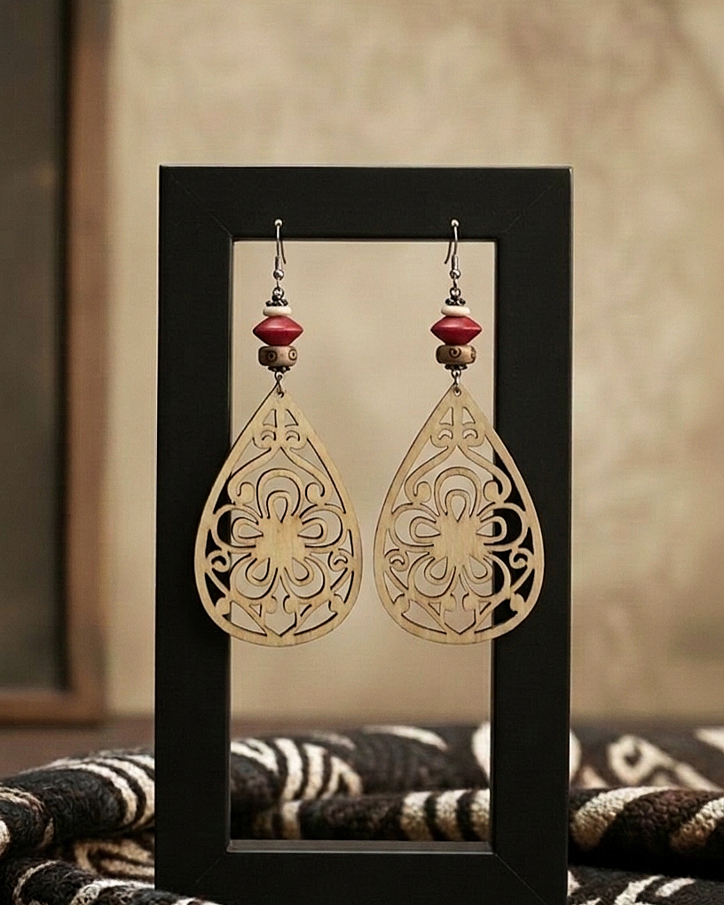 Pair of gold filigree earrings with red beads on a black stand.