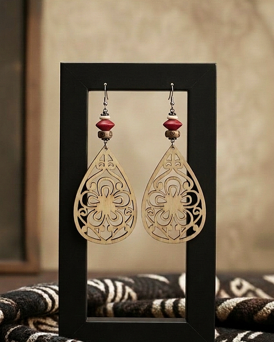 Pair of gold filigree earrings with red beads on a black stand.