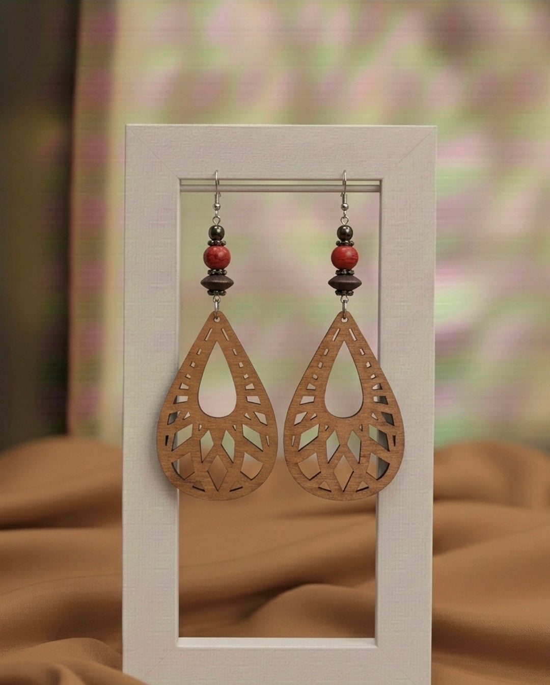 Wooden earrings with red beads on a display card against a blurred floral background