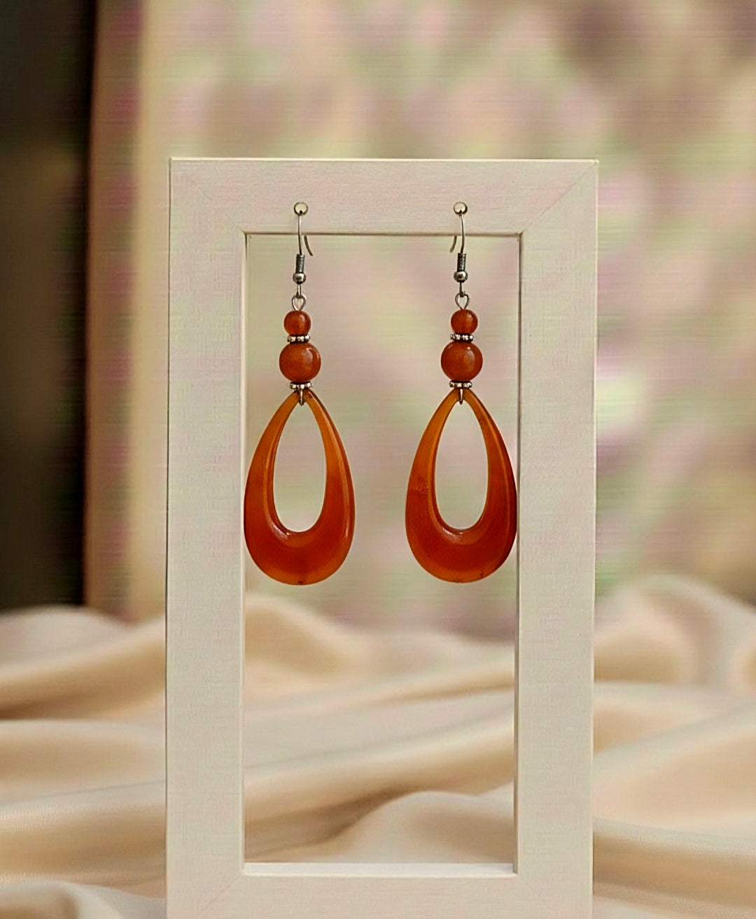 Pair of orange teardrop earrings with brown beads on a beige background