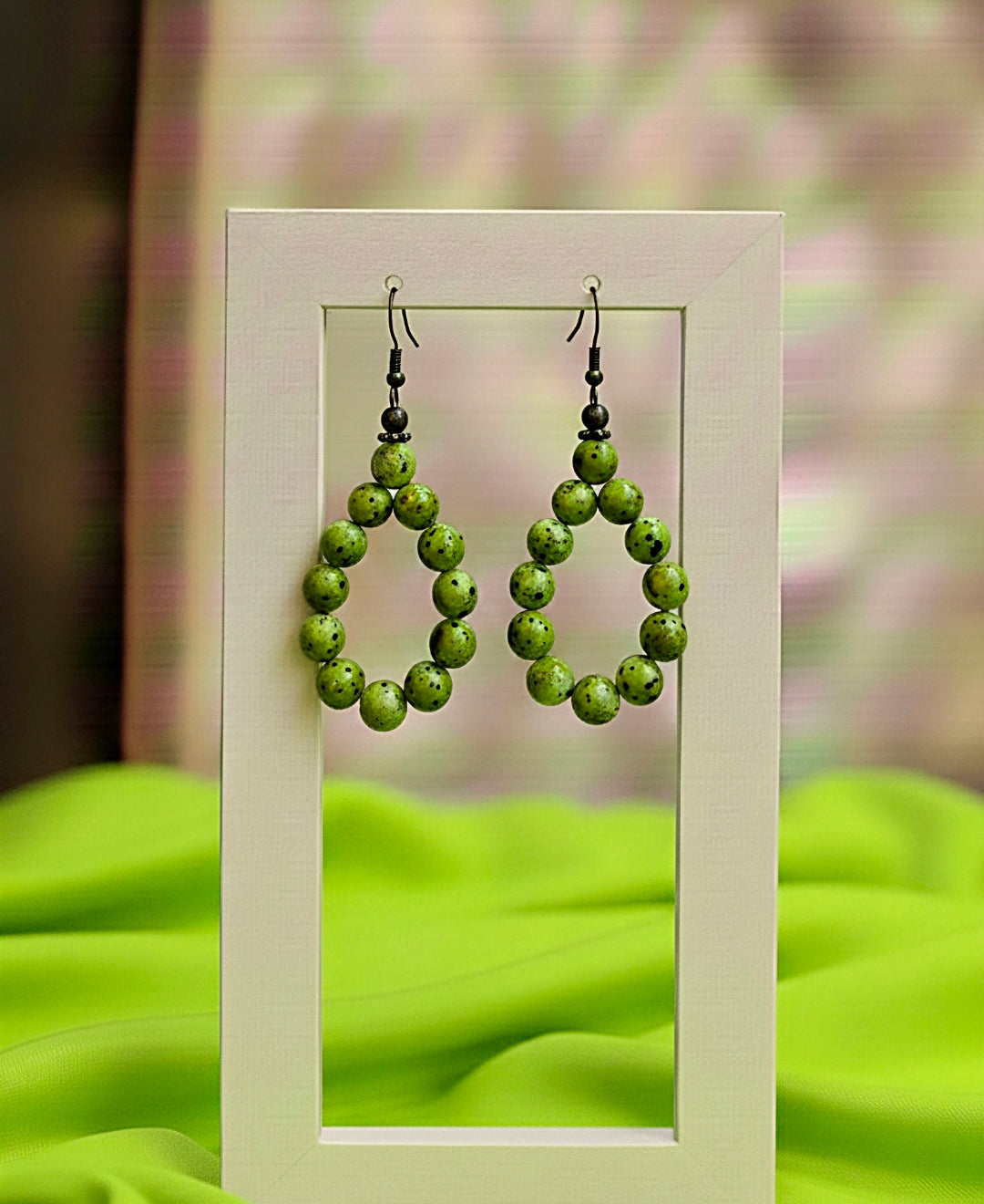 Green beaded earrings displayed against a green fabric background