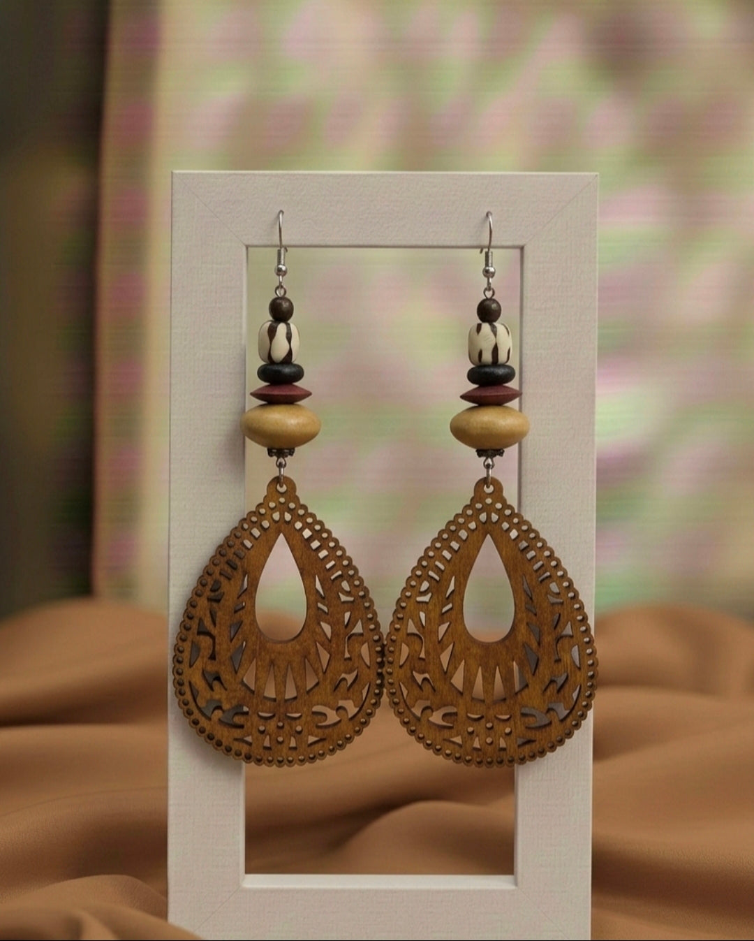 Pair of ornate earrings with wooden beads on a white card against a blurred background