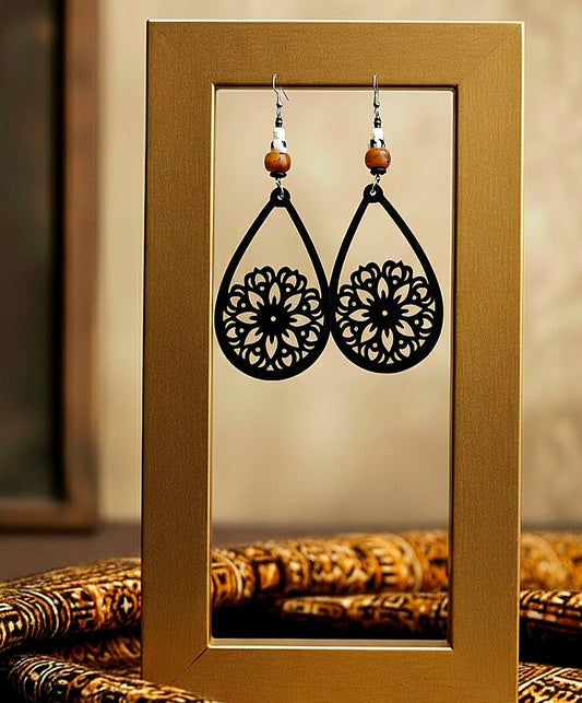 Black floral earrings on a gold display card with a blurred background