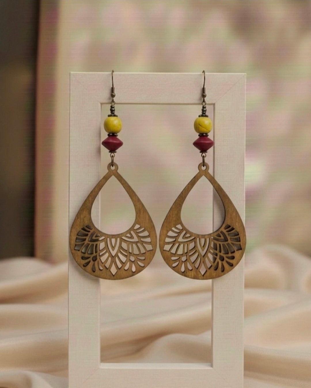 Pair of gold earrings with floral cut-out design on a beige background