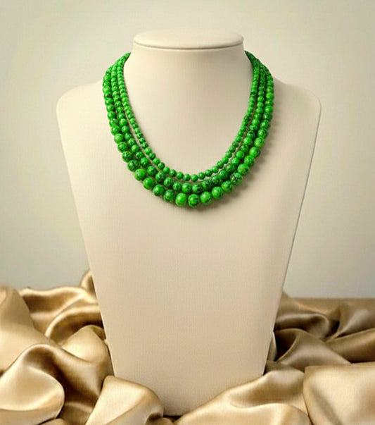 Green beaded necklace on a mannequin bust with a beige fabric background