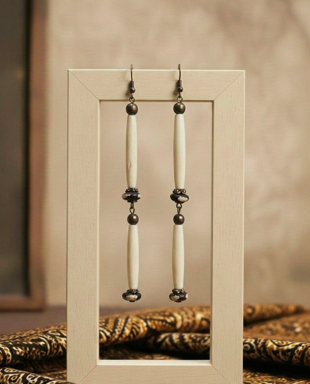 Pair of earrings with long beige African bone beads and black beads displayed in a wooden frame.