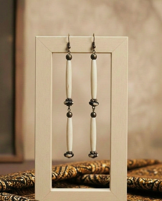 Pair of earrings with long beige African bone beads and black beads displayed in a wooden frame.