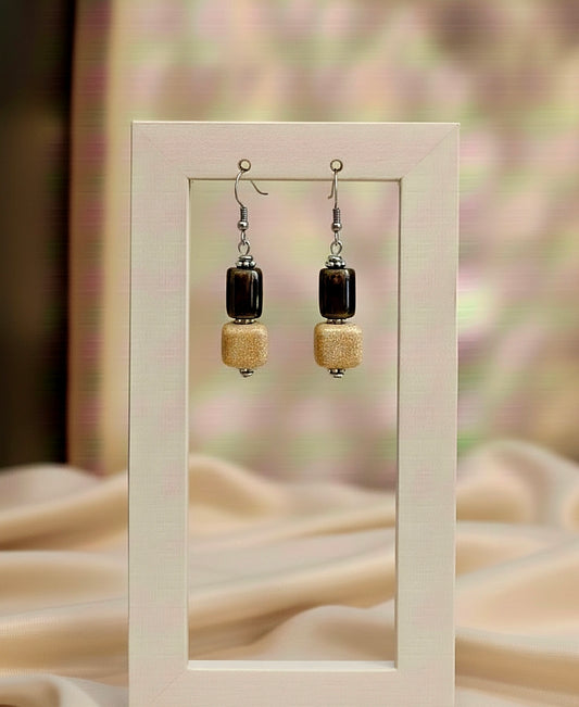 Pair of earrings with black and beige beads displayed in a white frame.