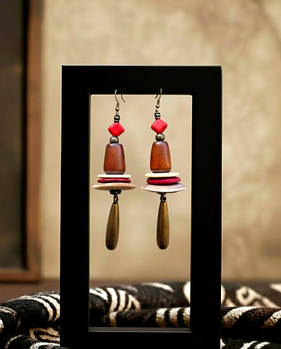 Pair of earrings with red and brown beads on a black stand against a neutral background