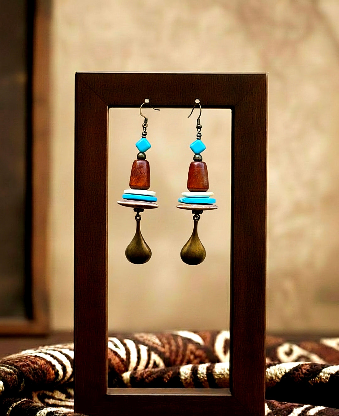 Pair of earrings with wooden and turquoise beads displayed in a wooden frame.