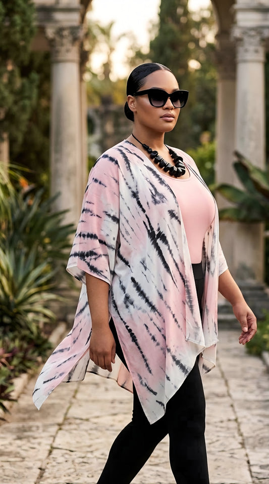 A woman walking outdoors in a garden courtyard wearing a pink, black, and white tie-dye kimono cardigan over a pink top and black pants.